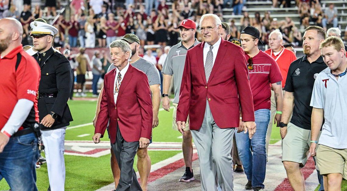 Dr. Jack Hawkins, Jr. walking on thee field at Veteran's Memorial stadium with members of the military. 